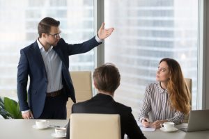 Harassment and retaliation exemplified by an angry man gesticulating at seated woman. 